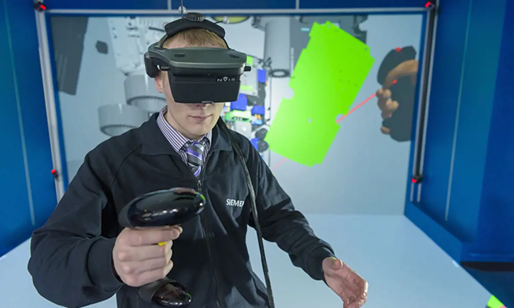A person with a siemens jacket on wearing a virtual reality headset and a handheld controller to practise engineering.