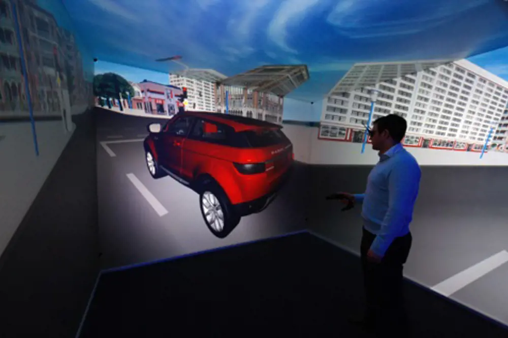 A person standing in a room where a 3D model of a Jaguar Land Rover is projected onto the walls. 