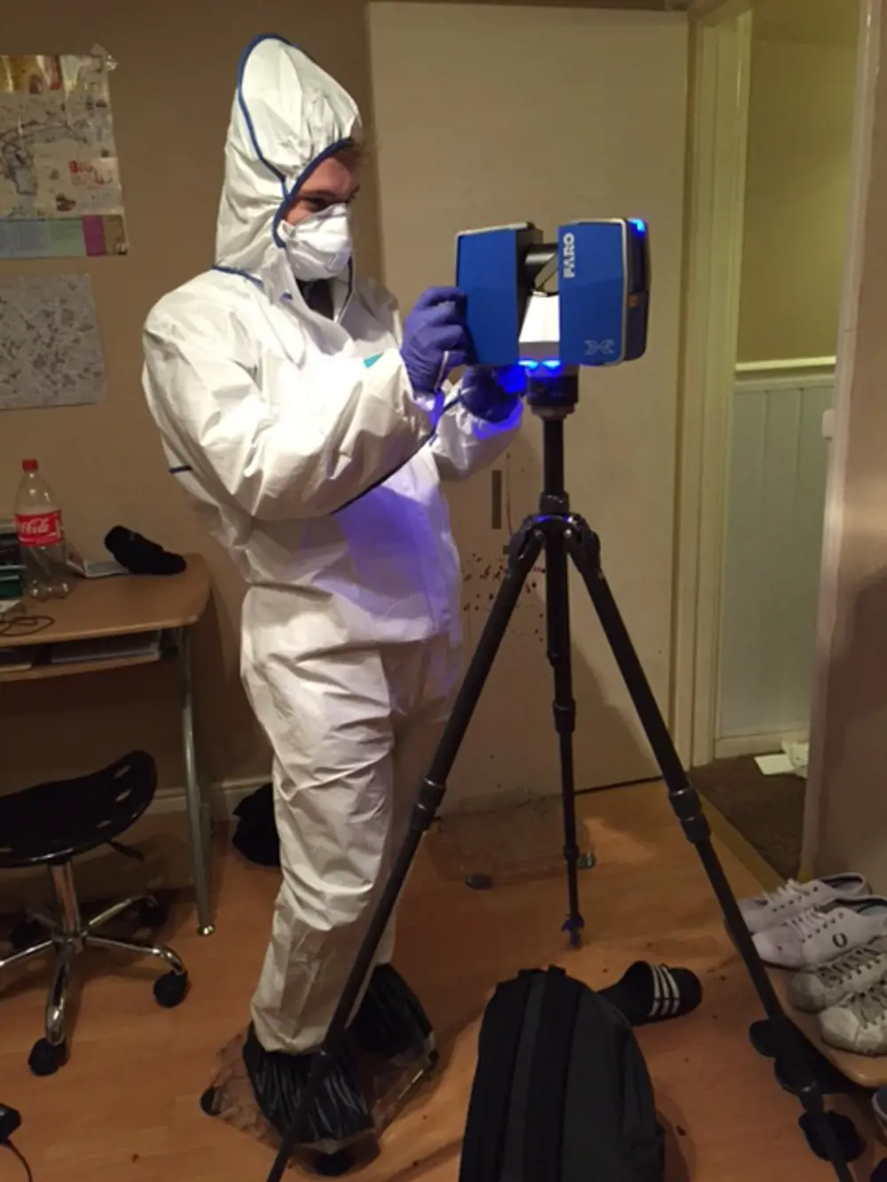 A person wearing a protective suit and mask adjusting a scene scanner in a room.