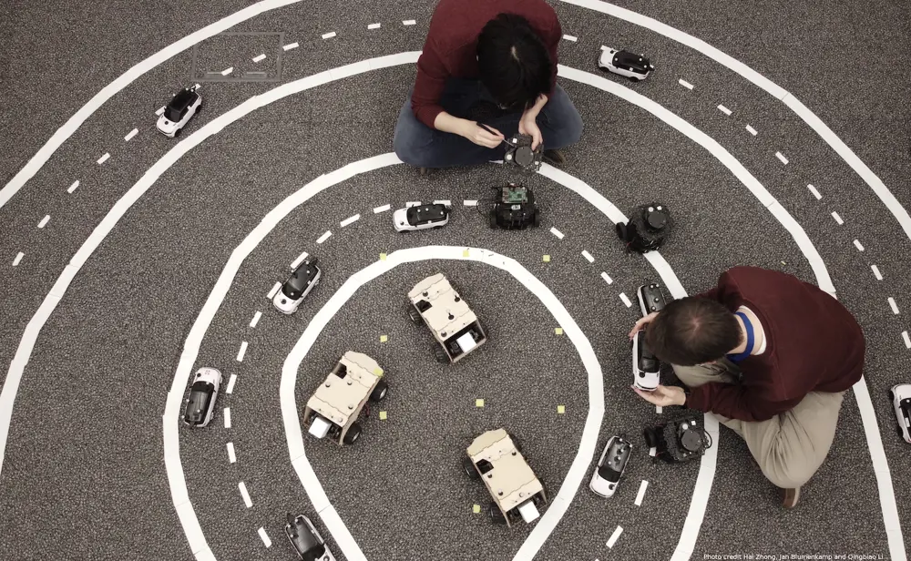 Two robotics engineers are viewed from above as they set up an experiment on miniature autonomous robotic cars.