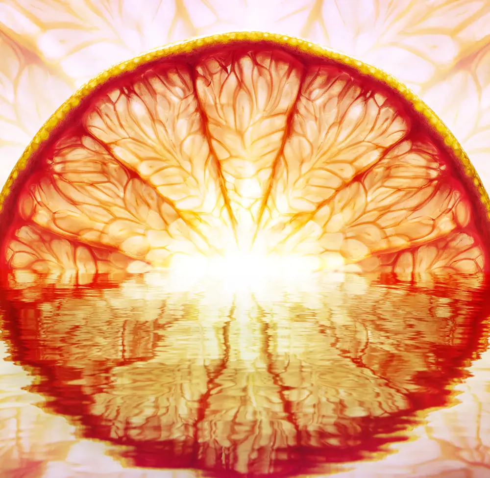 A close-up shot of half an orange segment that is reflected in water, looking like a sunrise