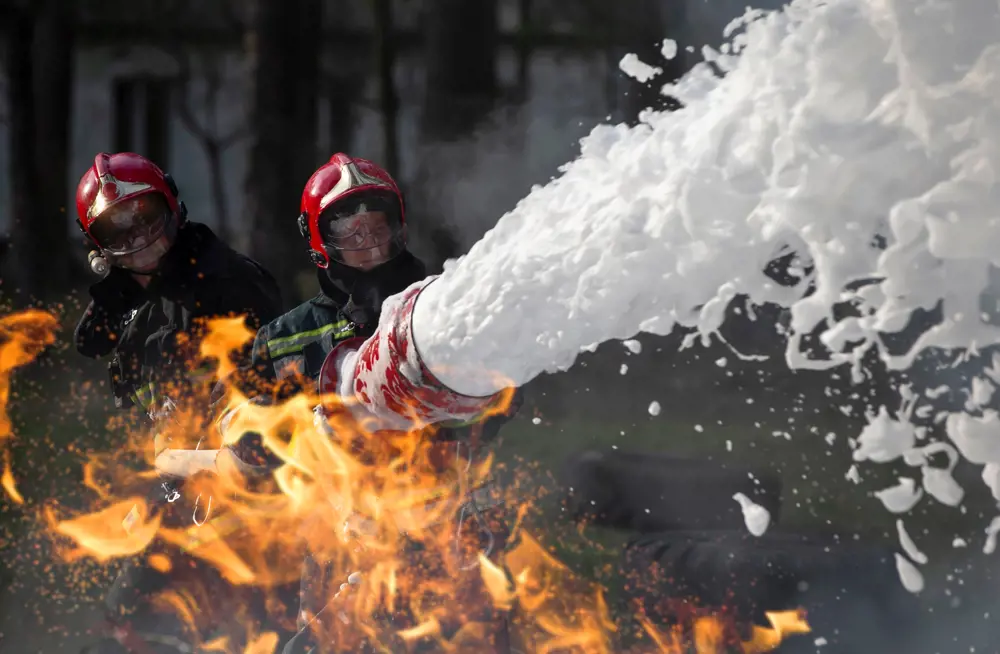 Firefighters spraying a fire with an aqueous film forming foam, which in the past has been a source of forever chemical pollution.
