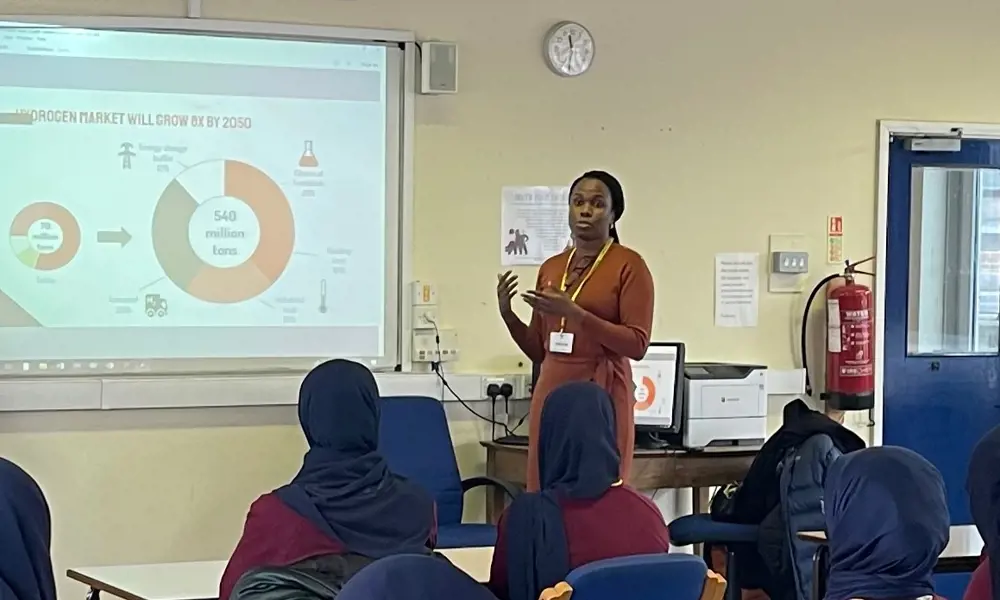 A woman standing at the front of a classroom, telling young people about STEM.