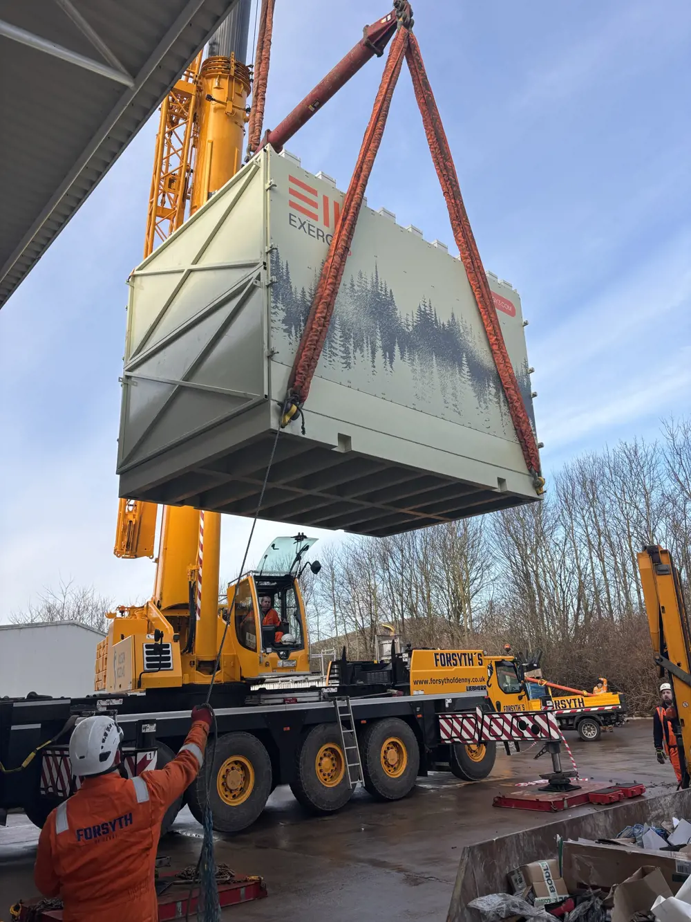 A large light grey shipping container is suspended from a crane.