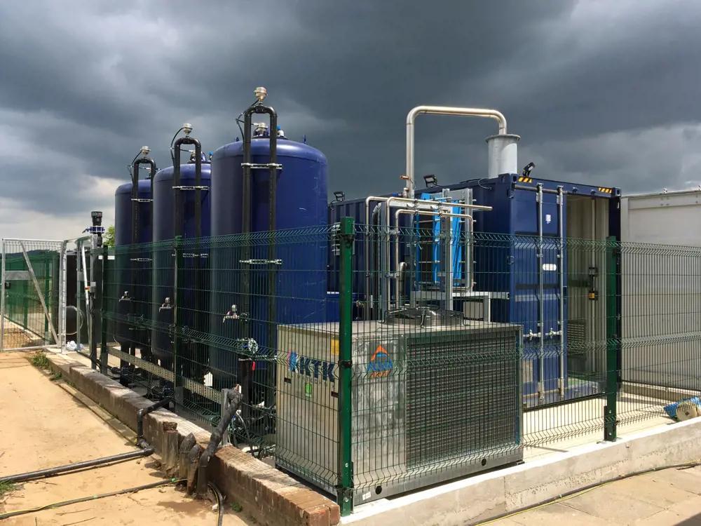 A water remediation treatment facility, comprising several large tanks and pipes connected to a shipping container.