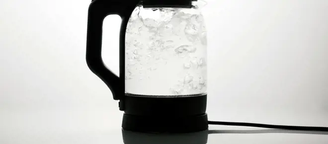 A transparent electric kettle boiling water which is bubbling inside. 