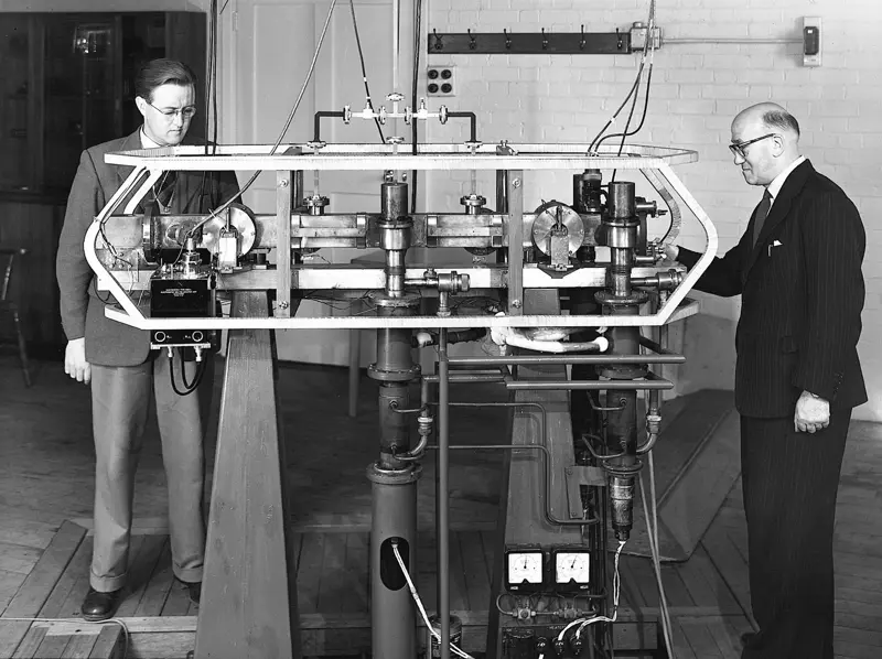 A greyscale image of two men standing next to the first accurate atomic clock.