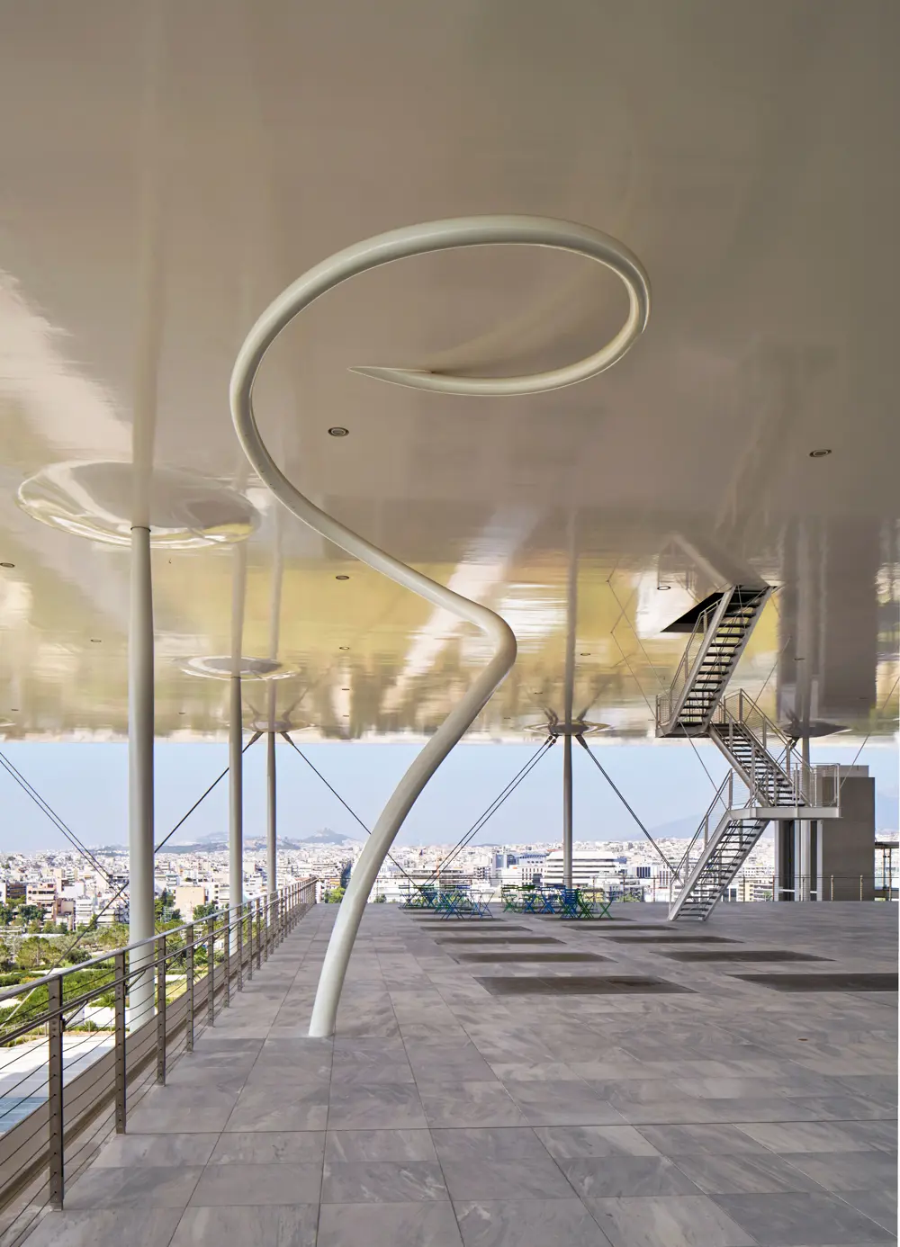 A white thin spiral structure going down from a ceiling to a floor.