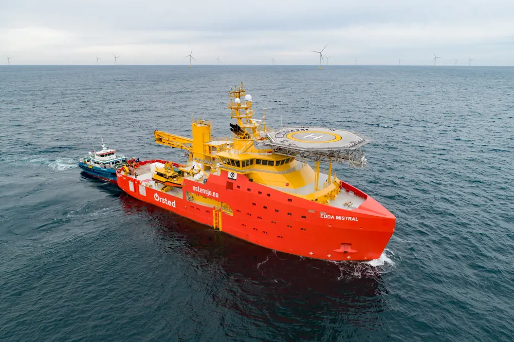 An Orsted ship in the ocean with wind turbines in the background.