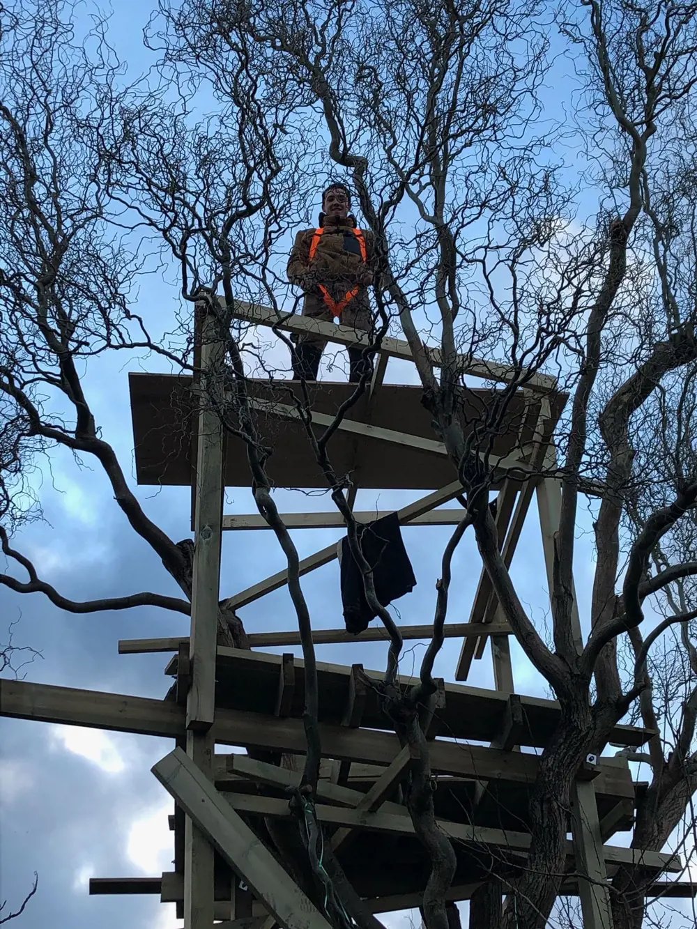 A playground engineer in a high vis jacket, standing on top of a wooden playground installation being built.