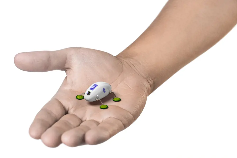 A photograph of a swarm robot in the palm of a hand which resembles the body of an insect. It has a small camera at the front and four miniature 'legs'.