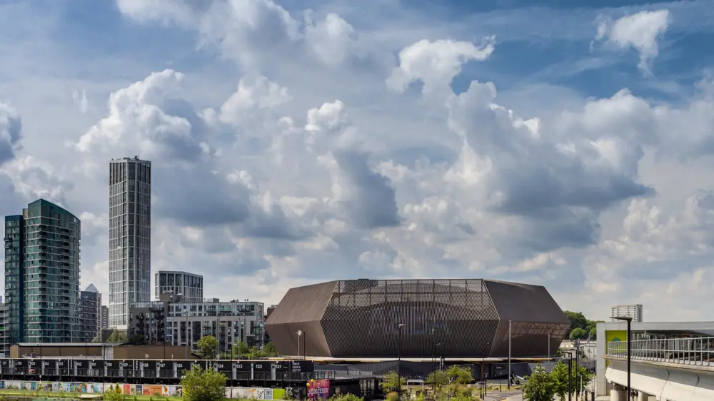 A wooden framed stadium seen next to skyscrapers with rolling clouds on a bright day