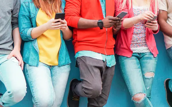 Five people from the neck down holding mobile phones. 