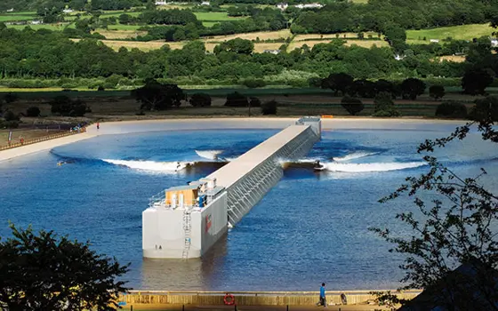A large body of water outside with a wave generator and surfers.
