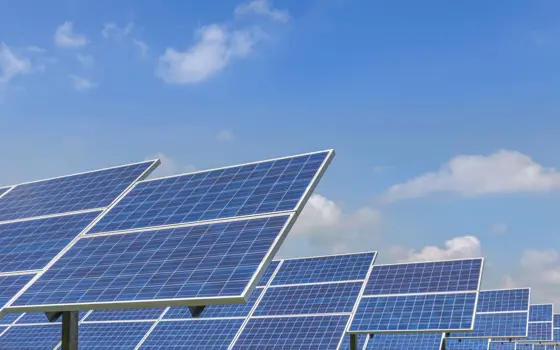 Large solar panels pictured on ground frames on a solar farm, with a blue, slightly cloudy sky above.
