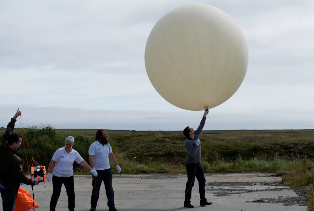 A person holding a large circular high-altitude floating balloon that is ready to be launched. 