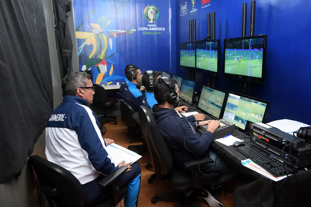 Video assistant referee (VAR) team monitoring multiple screens during a football match review in a control room.