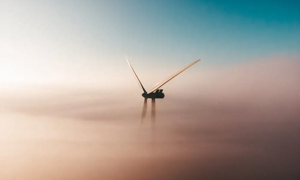 The top of a wind turbine peaking through orange mists in the sky.