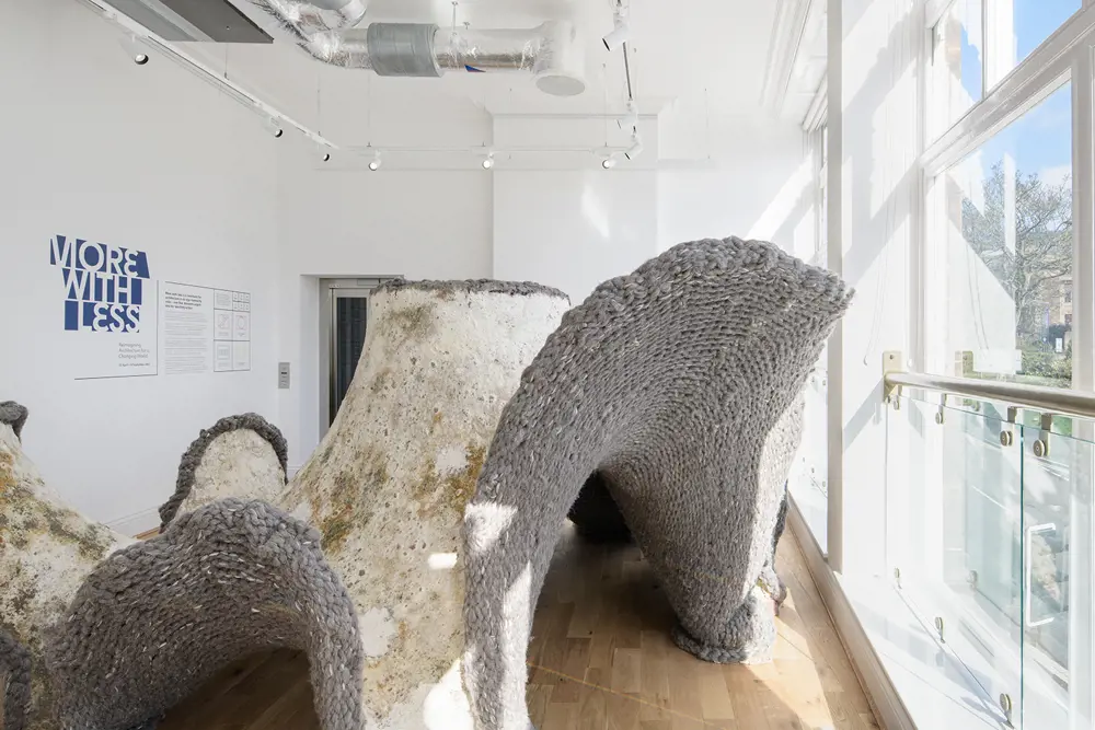 An organically shaped structure that fills a room, made from grey wool and white mycelium that has grown onto the wool.