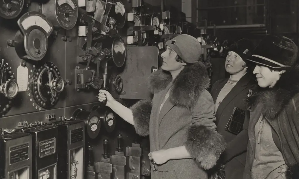 A monochrome photograph of three women on a tour of an early power station.