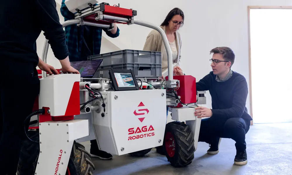Team inspecting and adjusting a Saga Robotics agricultural robot carrying a storage crate on top.