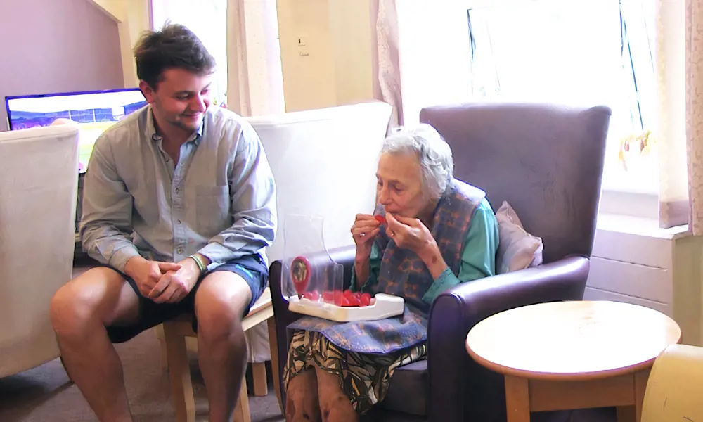 A young mang sitting with his grandma, who is eating a red Jelly Drop sweet