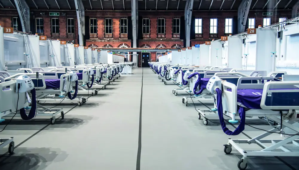 A large Victorian hall that includes rows of hospital beds with purple mattresses