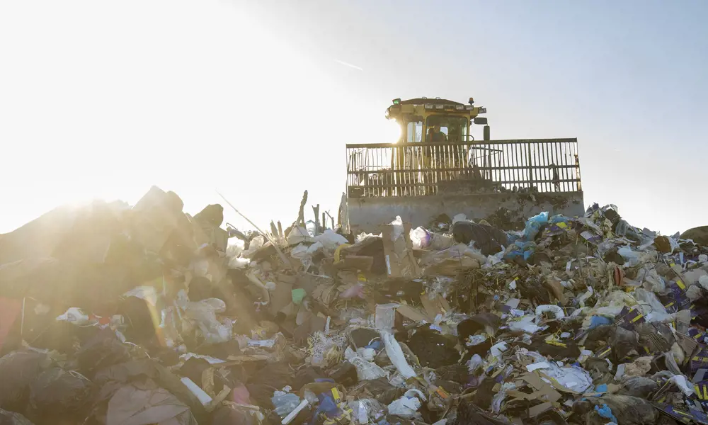 A tractor on top of a pile of rubbish at a landfill site.