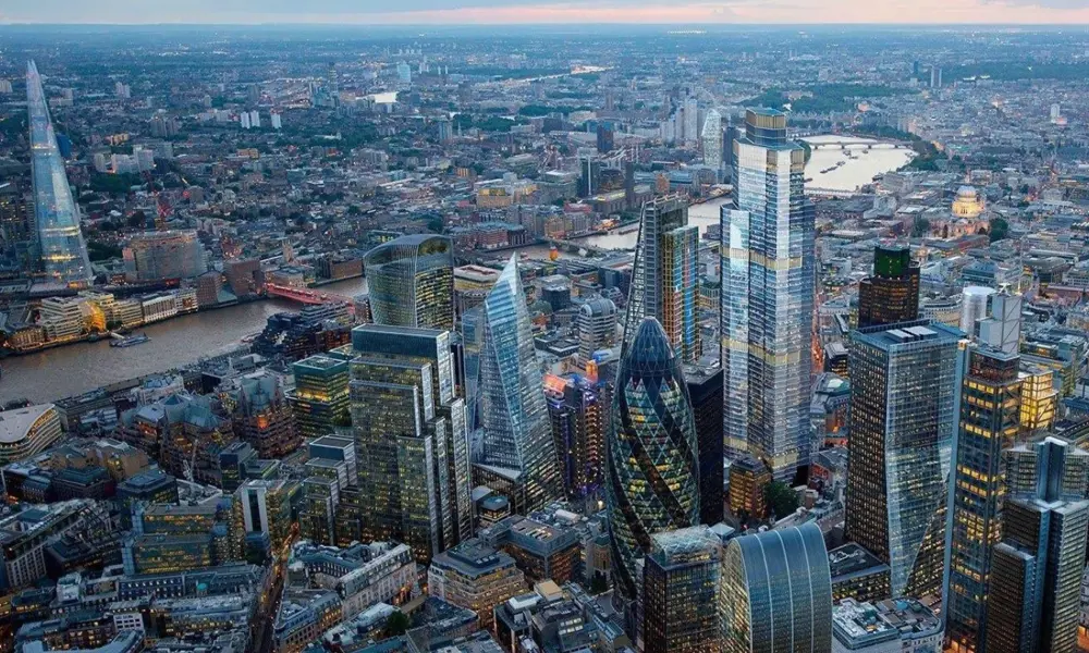 An aerial view of London's skyscraper buildings in the foreground with the River Thames behind them.