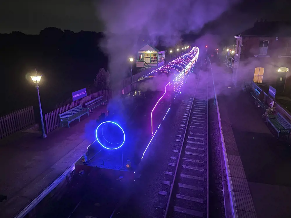 A steam train seen from above lit up with LED lights in white, blue, and red