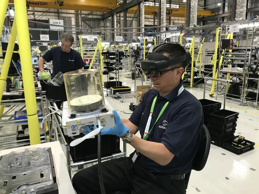 A person with goggles on sitting down in a factory and holding a part of a ventilator.