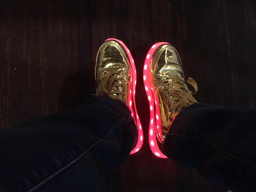 A photo of gold trainers which have a pink fluorescent light around the base.