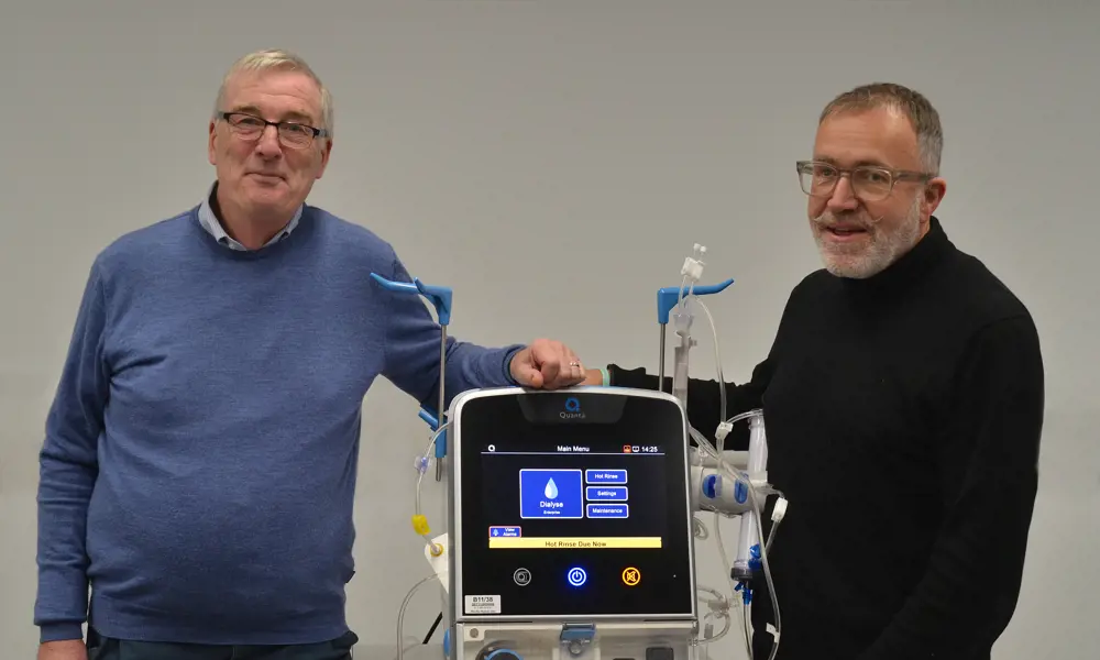 Two men stand either side of a dialysis machine