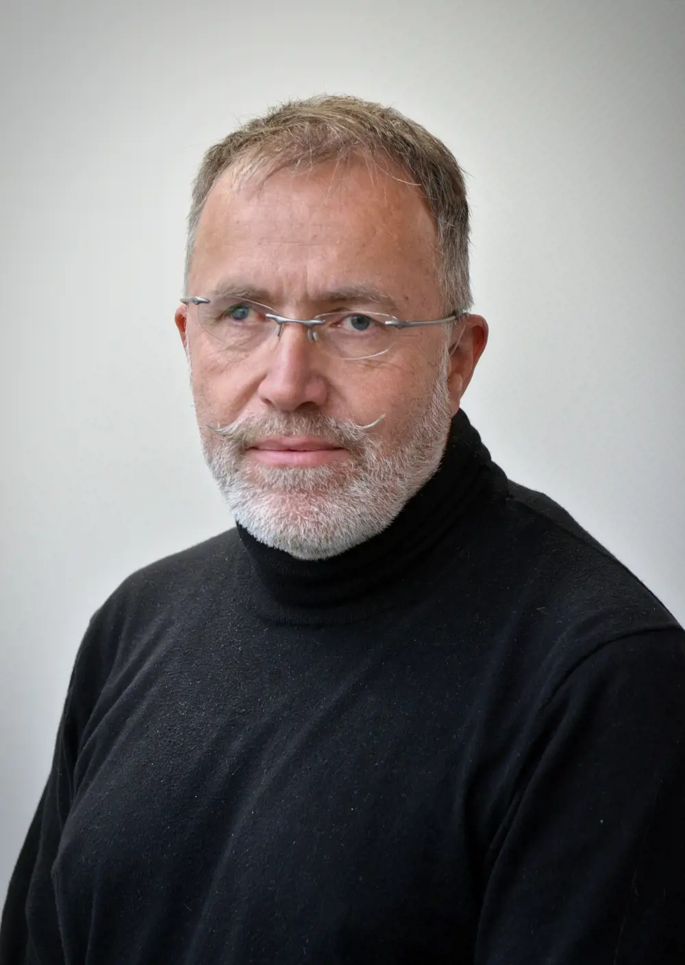 A man wearing glasses and a black top looks at the camera