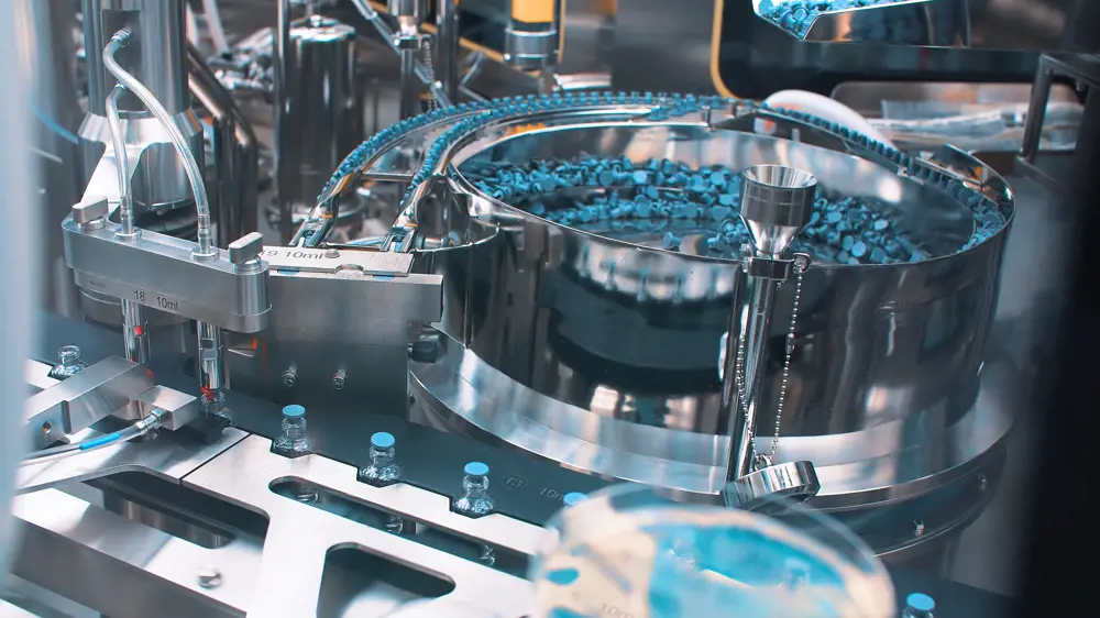 A close up of a machine, which is placing liquid into clear vials and then the vials are being sealed with lids in an automatic process.