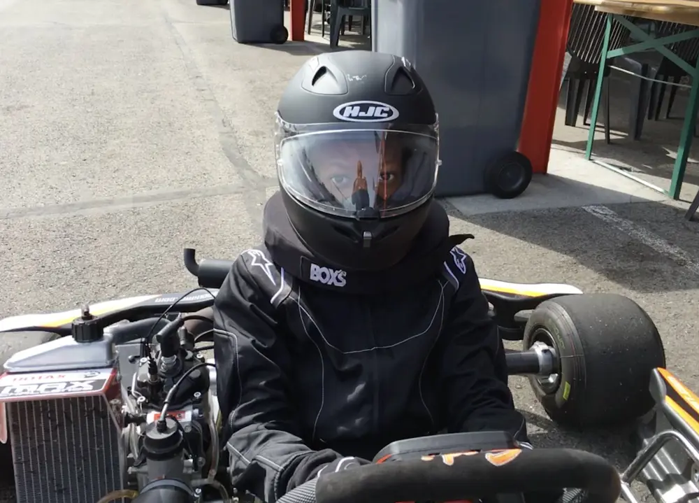 A close up of a teenage boy sitting in a racing kart, wearing a helmet.