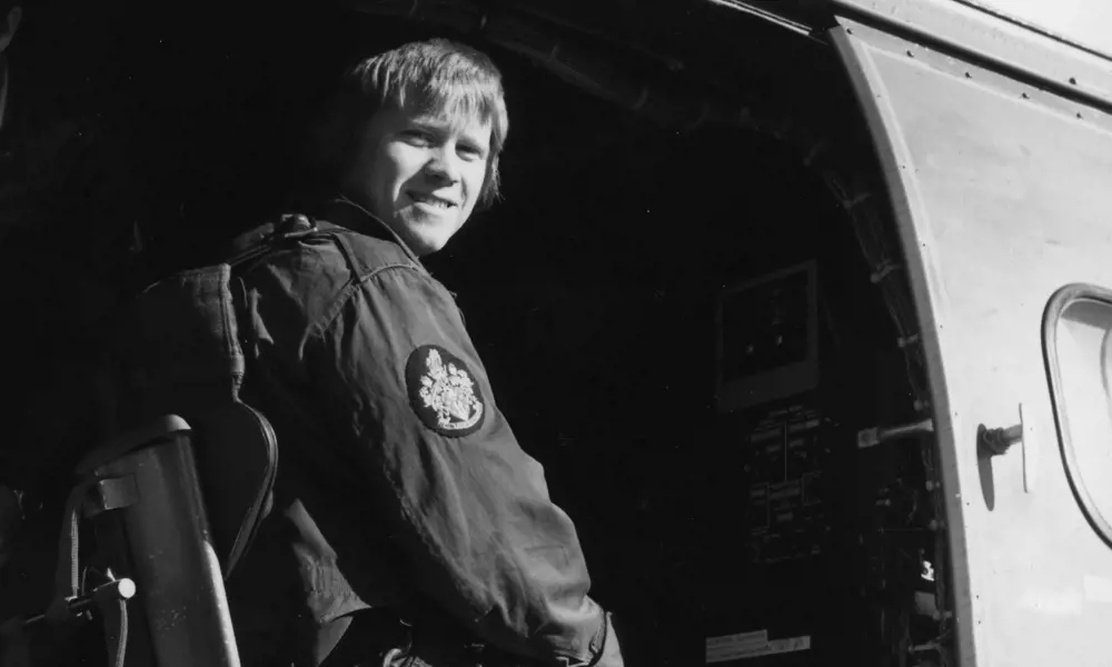 A black and white photograph of a young man sitting in a helicopter.