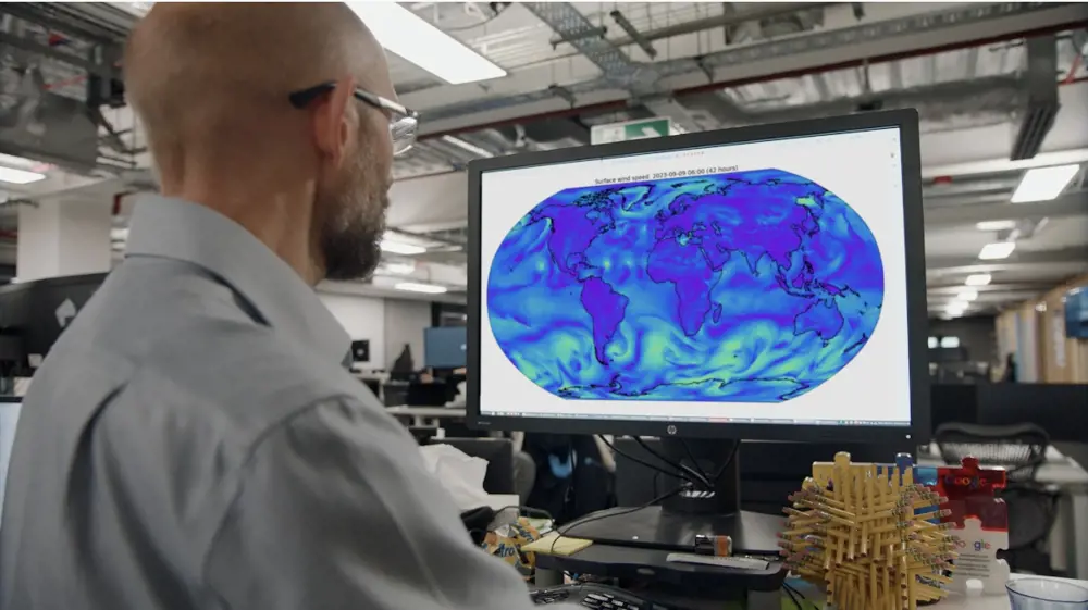 A data scientist with glasses looking at a visualisation of weather swirling in green and blue overlaid on a world map