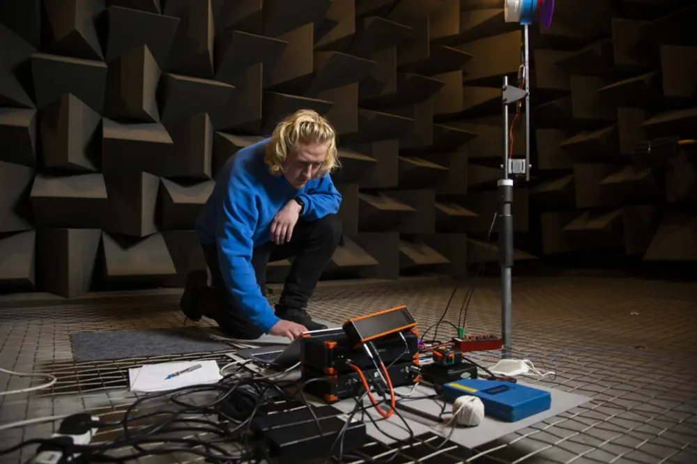 Person working with sound measurement equipment in an anechoic chamber lined with acoustic foam.