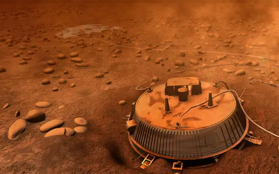 Artist’s impression of the Huygens probe resting on Titan’s rocky surface, with an orange haze and scattered stones under a thick atmosphere.