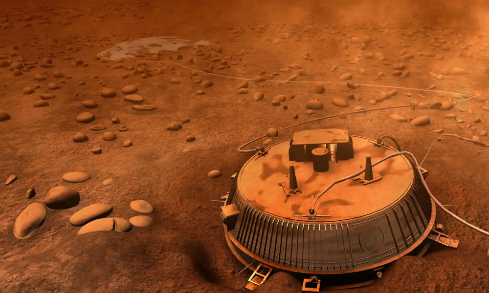 Artist’s impression of the Huygens probe resting on Titan’s rocky surface, with an orange haze and scattered stones under a thick atmosphere.