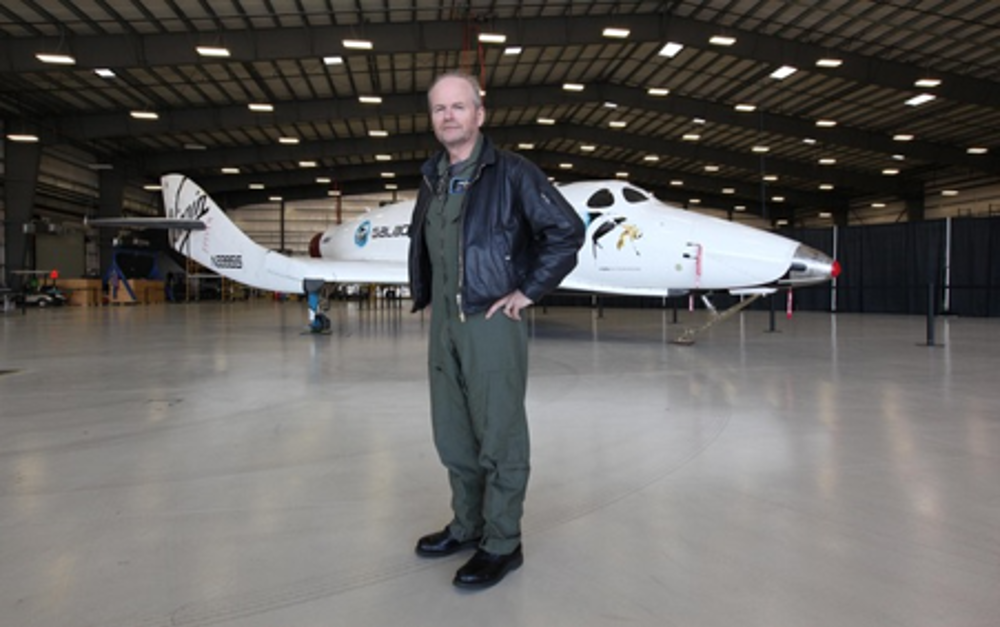 David Mackay standing in a hangar beside a white reusable spaceplane, highlighting commercial spaceflight development.