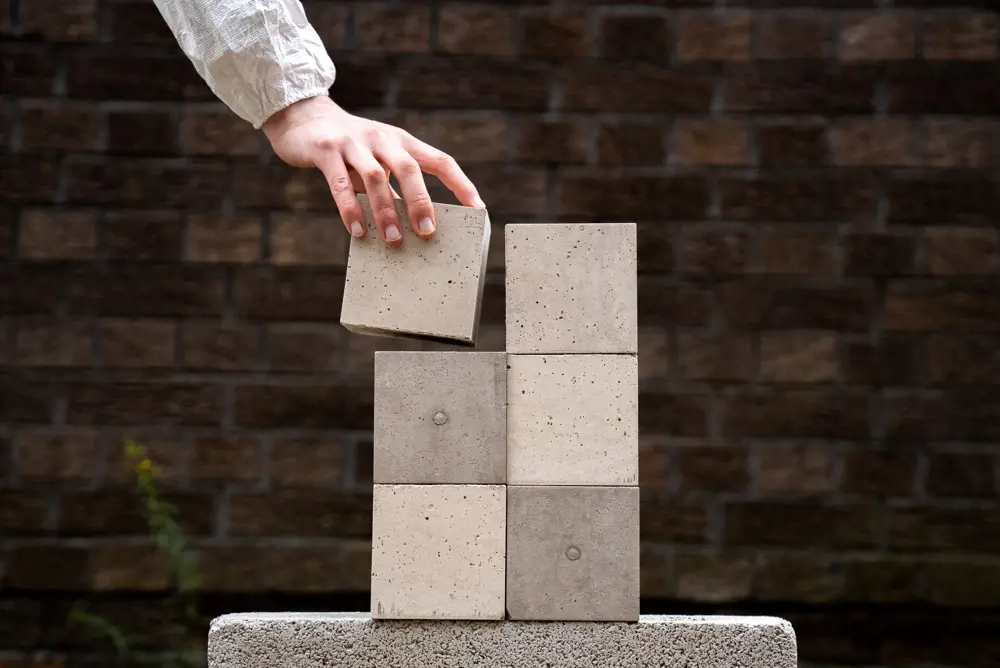 A hand places a small concrete block onto a stack of five others.