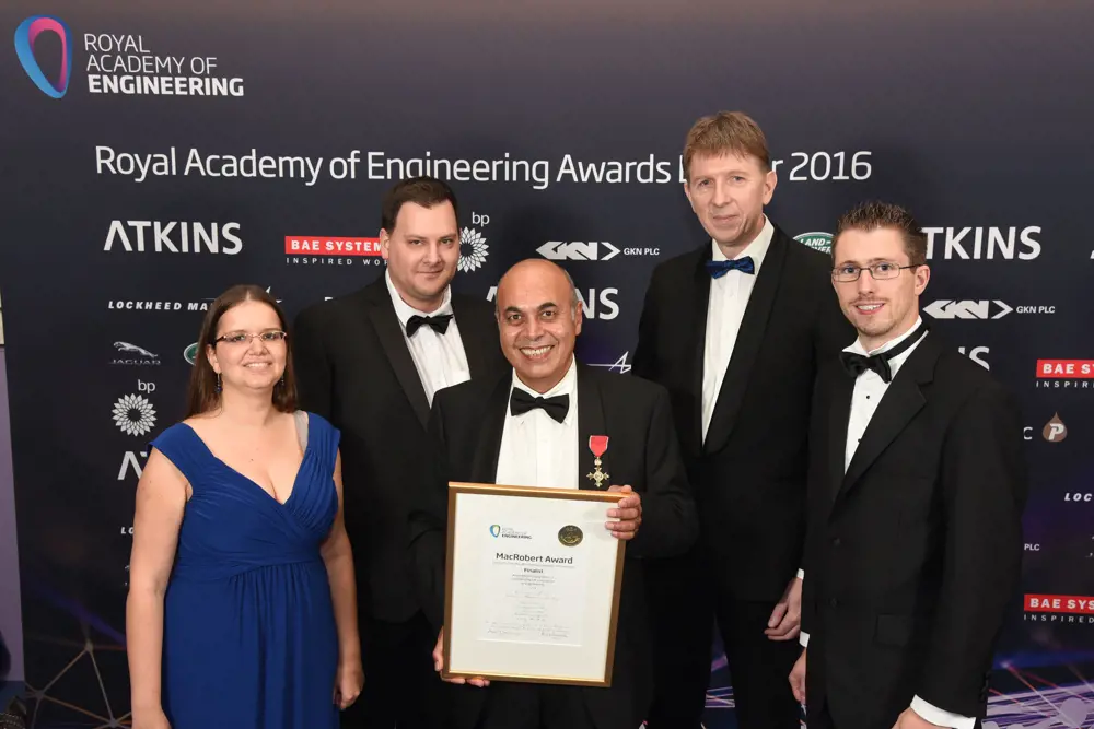 Professor Sir Saeed Zahedi OBE RDI FREng holding a framed MacRobert award standing in the middle of his Blatchford team at an awards ceremony. 