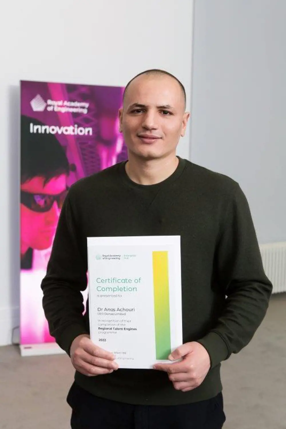 A man standing holding a certificate. It says "Certificate of Completion, as presented to Dr Anas Achouri, CEO of Donaa, in recognition of completing the Regional Talent Engines programme, 2022."