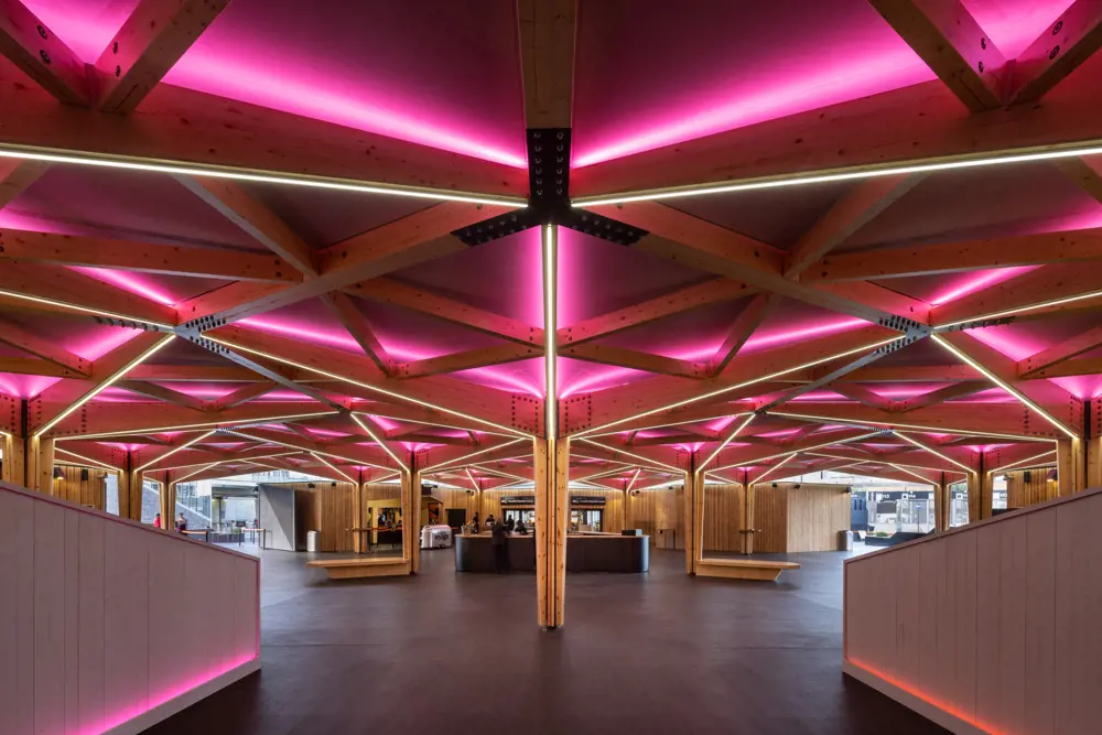 Pink glowing LED lights illuminate an intricately patterned timber frame in the lobby by a ticket desk