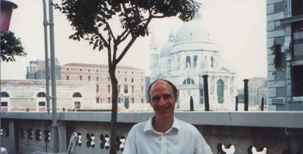 Stephen Temple smiling at the camera, with the top of the Basilica di Santa in Rome in the background. 