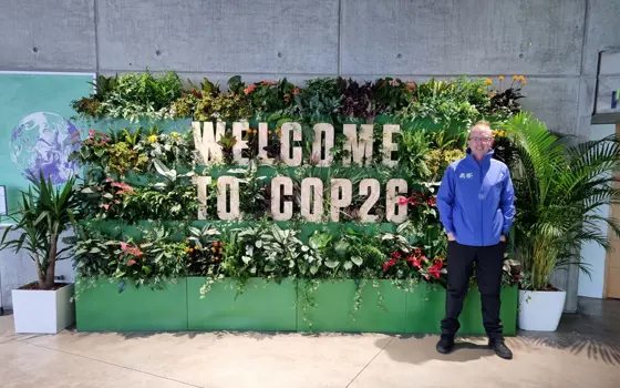 A man standing in front of a display that says "Welcome to COP26" on several shelves full of different plants.