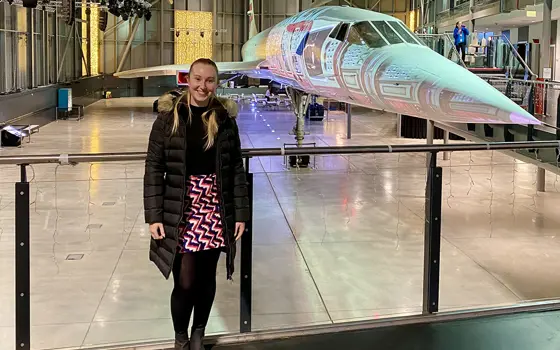 Person standing in a museum gallery beside a Concorde aircraft, with the plane’s nose and exhibition space visible behind.