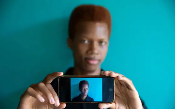 A person taking a live image of themselves with their phone. Their face can be seen behind the phone and also in the front screen of the phone taking a photograph.